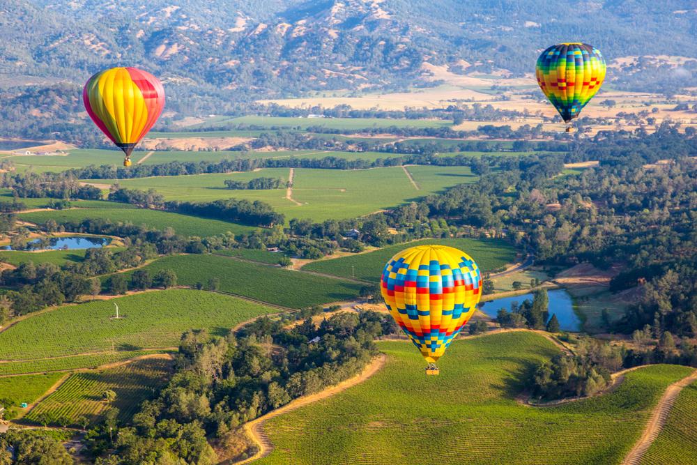 Hot air balloons over Napa Valley vineyards at dawn — sunrise flight above golden wine country hills
